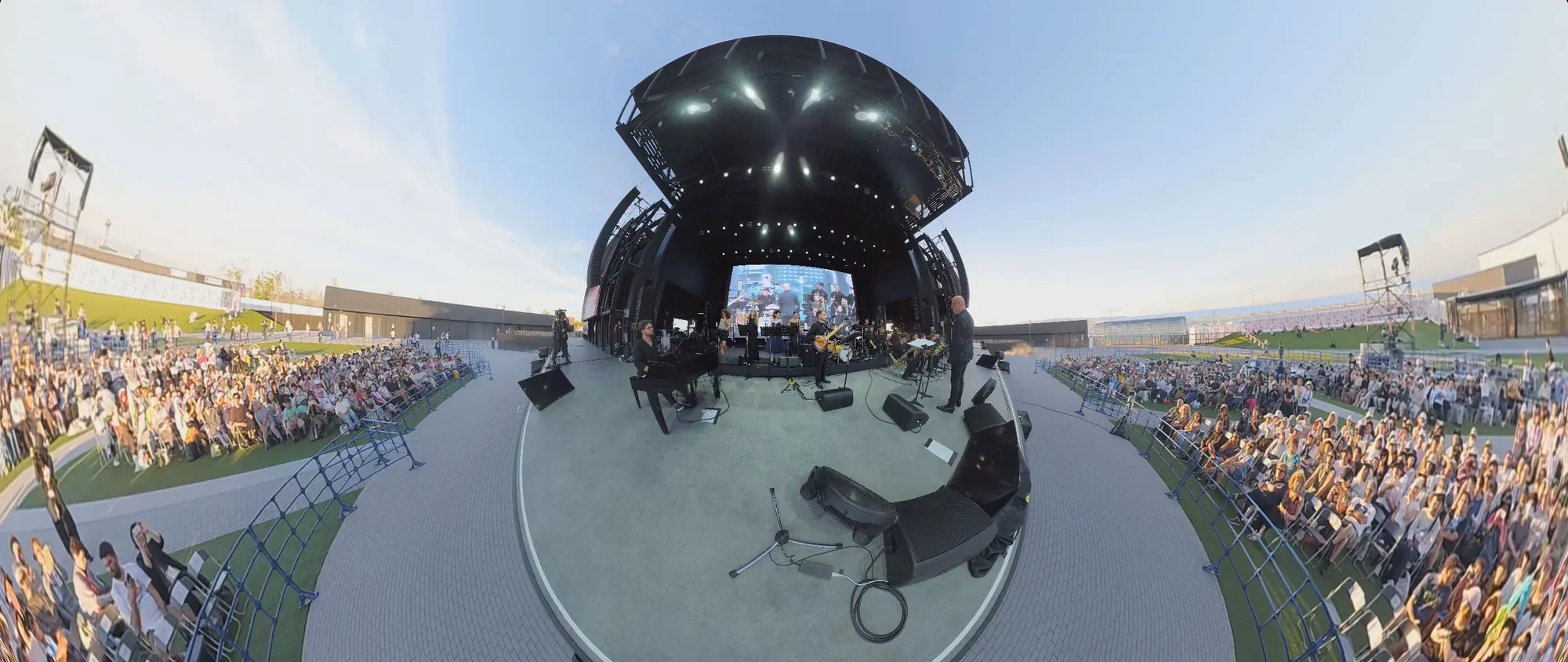 Una ripresa a 360° stesa in piano: al centro il palco dell’Arena Matsuri sotto la sua cupola, il pubblico sul prato da una parte e dall’altra, il cielo sopra.